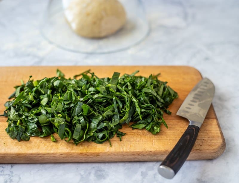 A knife slices through vibrant greens on a cutting board, preparing for the traditional Croatian recipe, Rudarska Greblica.