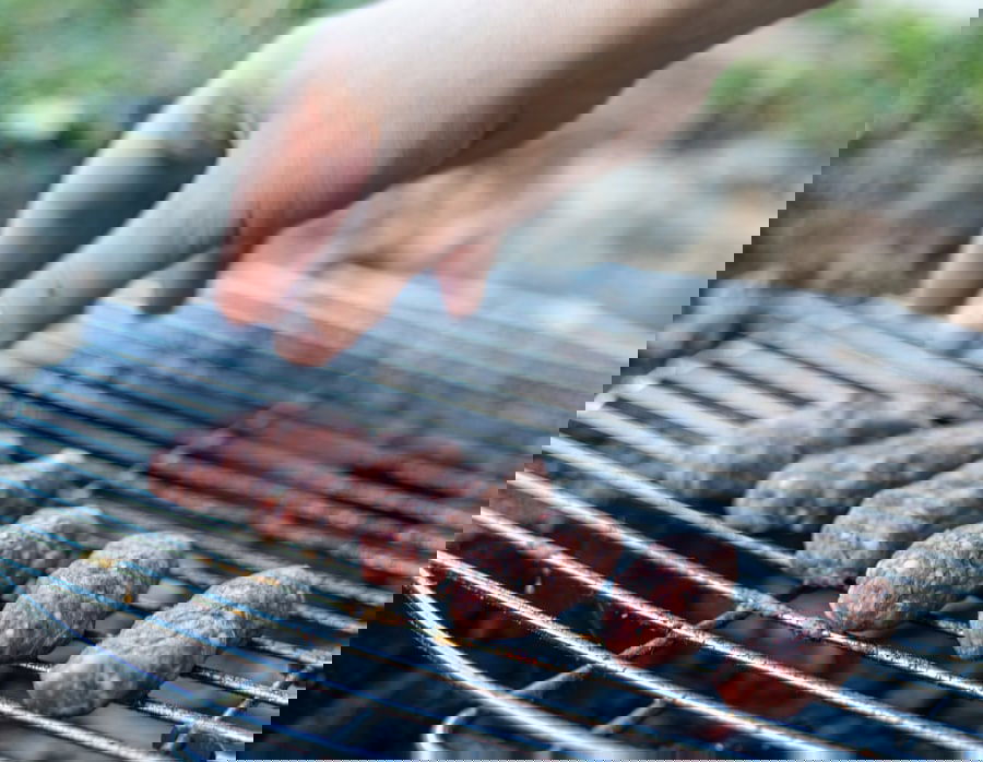 A person is grilling Sarajevski Ćevapi, which are skinless sausages.