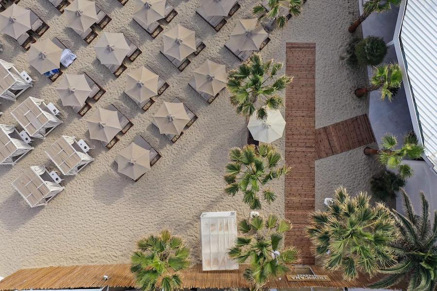 A tranquil aerial view of Mykonos beach with lounge chairs and umbrellas set up by beach clubs.