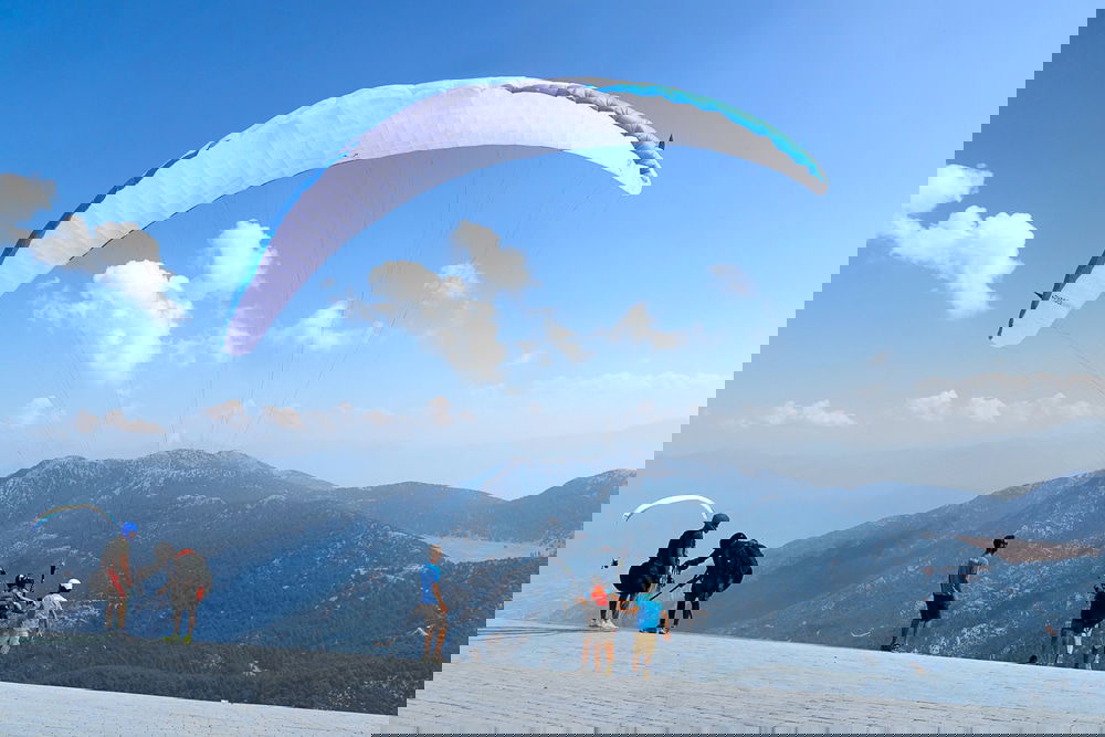 A group of people standing on top of Babadag Mountain with a paraglider, overlooking the breathtaking natural attractions in Turkey.