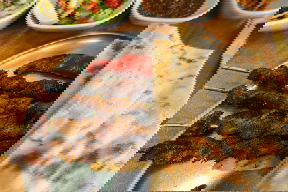 Diyarbakir Ciger Kebab and flatbread on a metal plate, with side dishes including salad, roasted pepper, sauces, and lemon wedges in the background—a true taste of Diyarbakir cuisine that any guide would recommend.